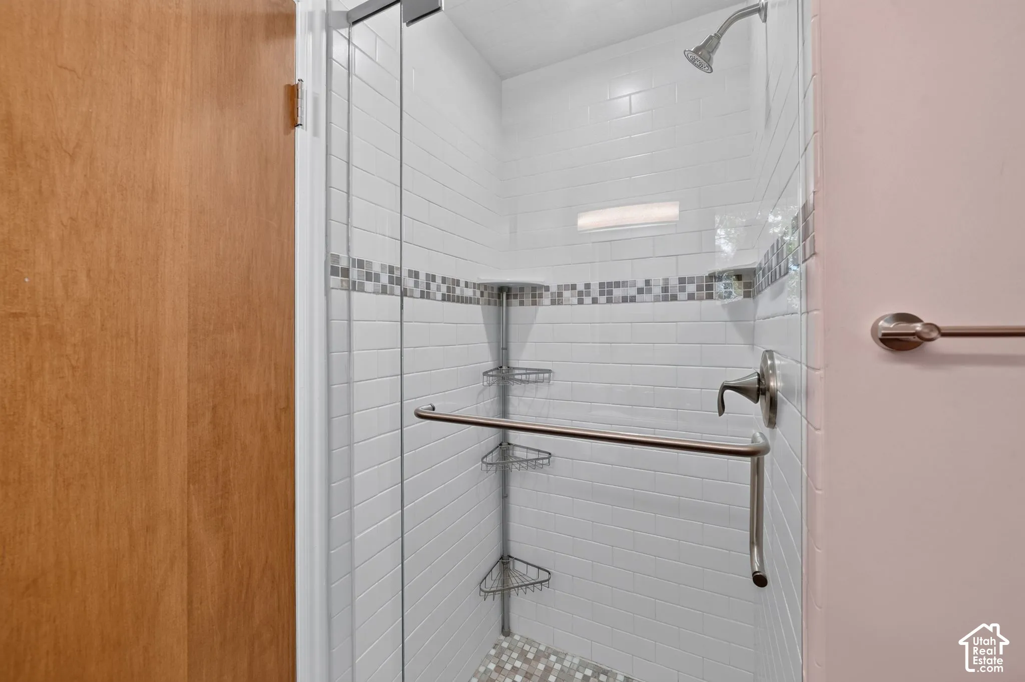 Tiled walk-in shower with a glass door and mosaic accent band in the primary bath.