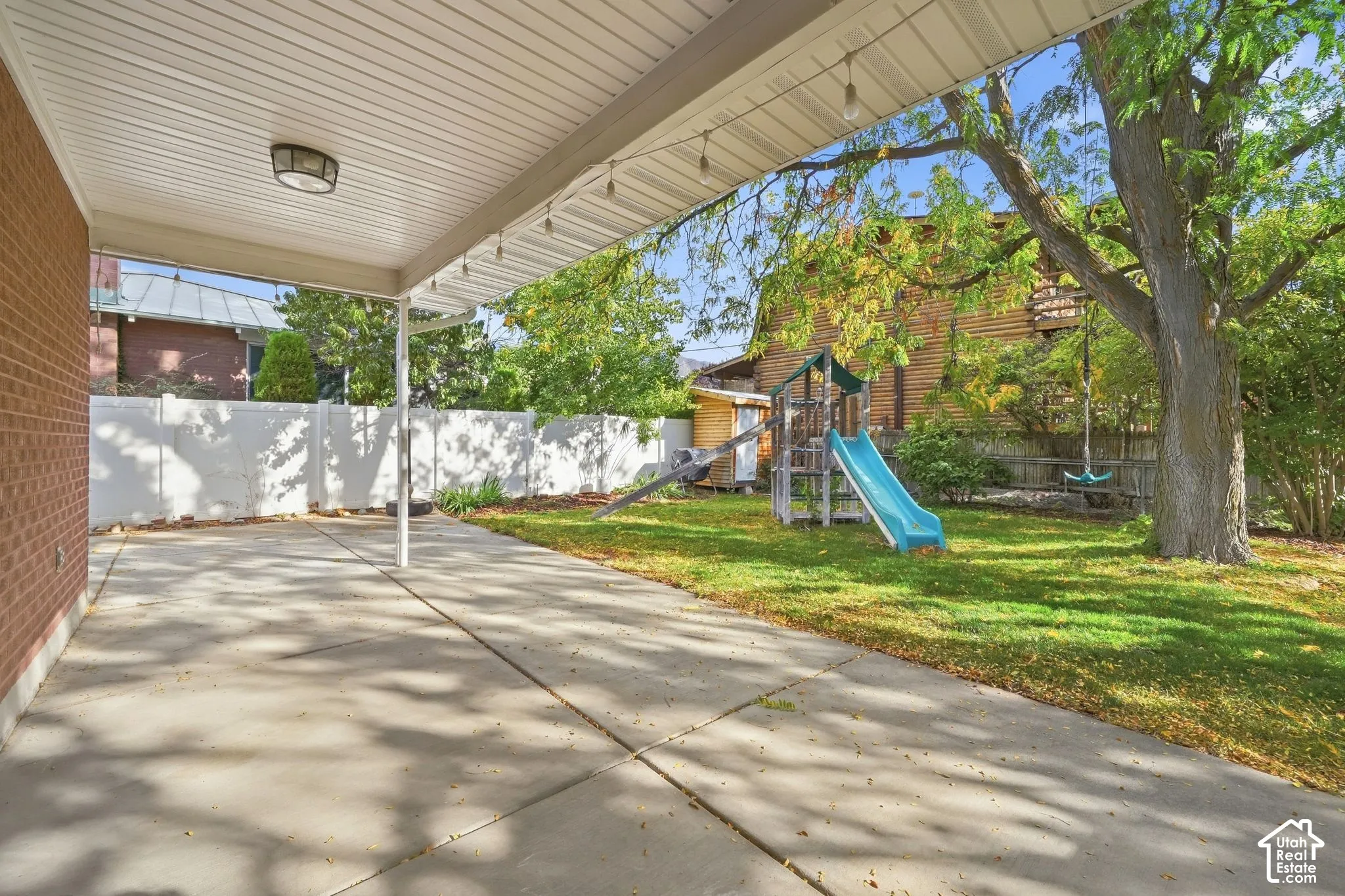 Covered patio looking out to the fenced yard, play structure, and trees.