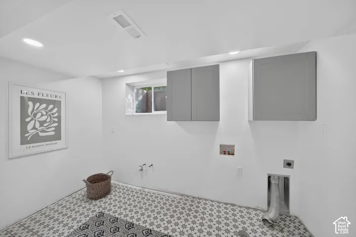 Laundry room with hookups, upper cabinets, and patterned tile floor.