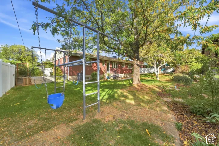 Secluded backyard with mature trees and a play structure behind the brick rambler.