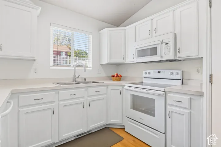 White cabinetry with panel doors, stainless steel double basin sink, white built-in microwave, white electric range, and light-toned countertops