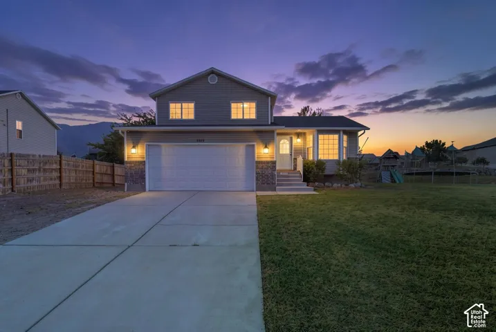 Two-story home with contemporary exterior featuring illuminated windows, attached two-car garage with concrete driveway, and manicured lawn with mature landscaping
