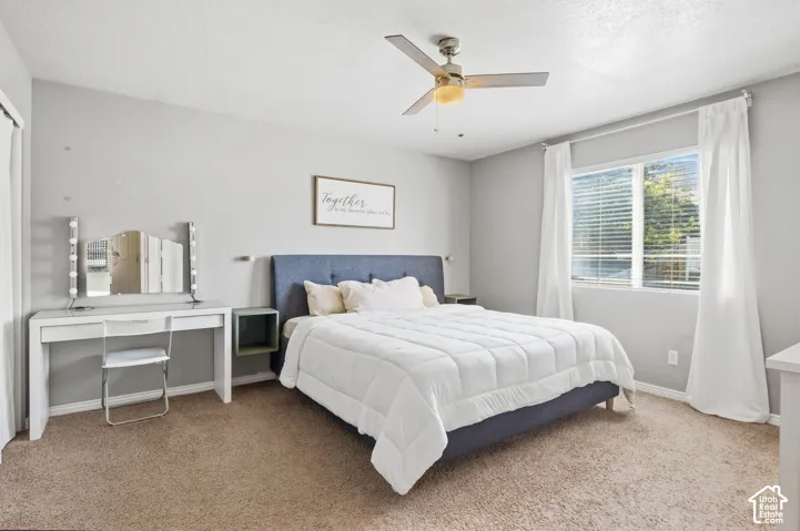 Light gray wall paint, brown carpet flooring, ceiling fan with integrated light, large window with horizontal blinds, built-in closet