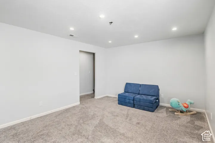 Recessed lighting illuminates the room, featuring light gray walls and plush gray carpeting