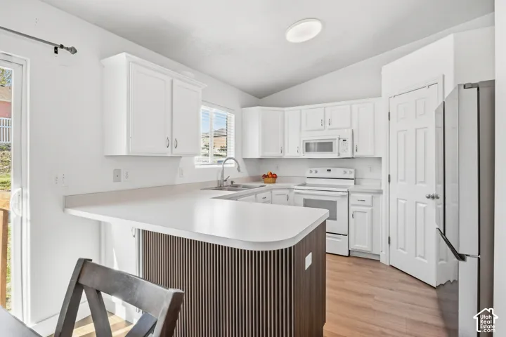 White cabinetry, stainless steel appliances, wood-finish flooring, vaulted ceiling, and a kitchen island with a breakfast bar