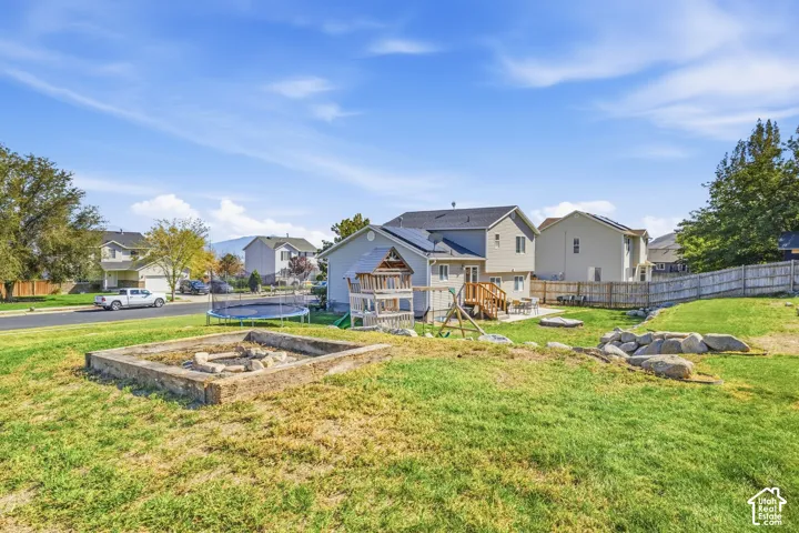 Expansive backyard featuring a stone-lined fire pit, wooden play structure, and mature landscaping