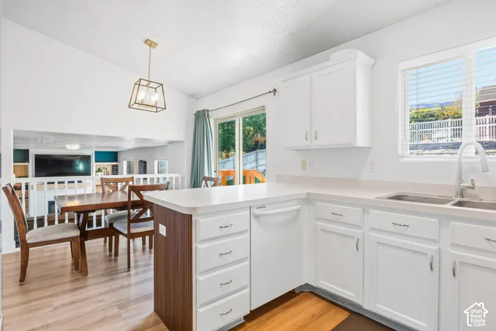 White cabinetry with a double basin sink, light-toned countertops, and wood-finish flooring