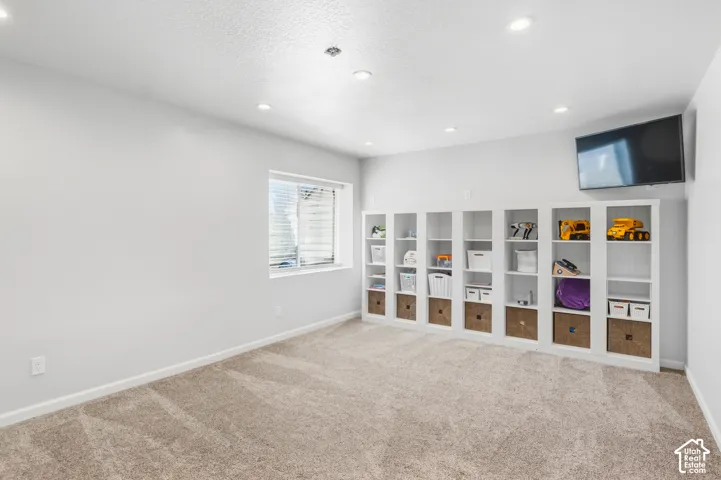 Neutral wall paint, recessed lighting, wall-to-wall carpeting, built-in shelving units, and a window with blinds