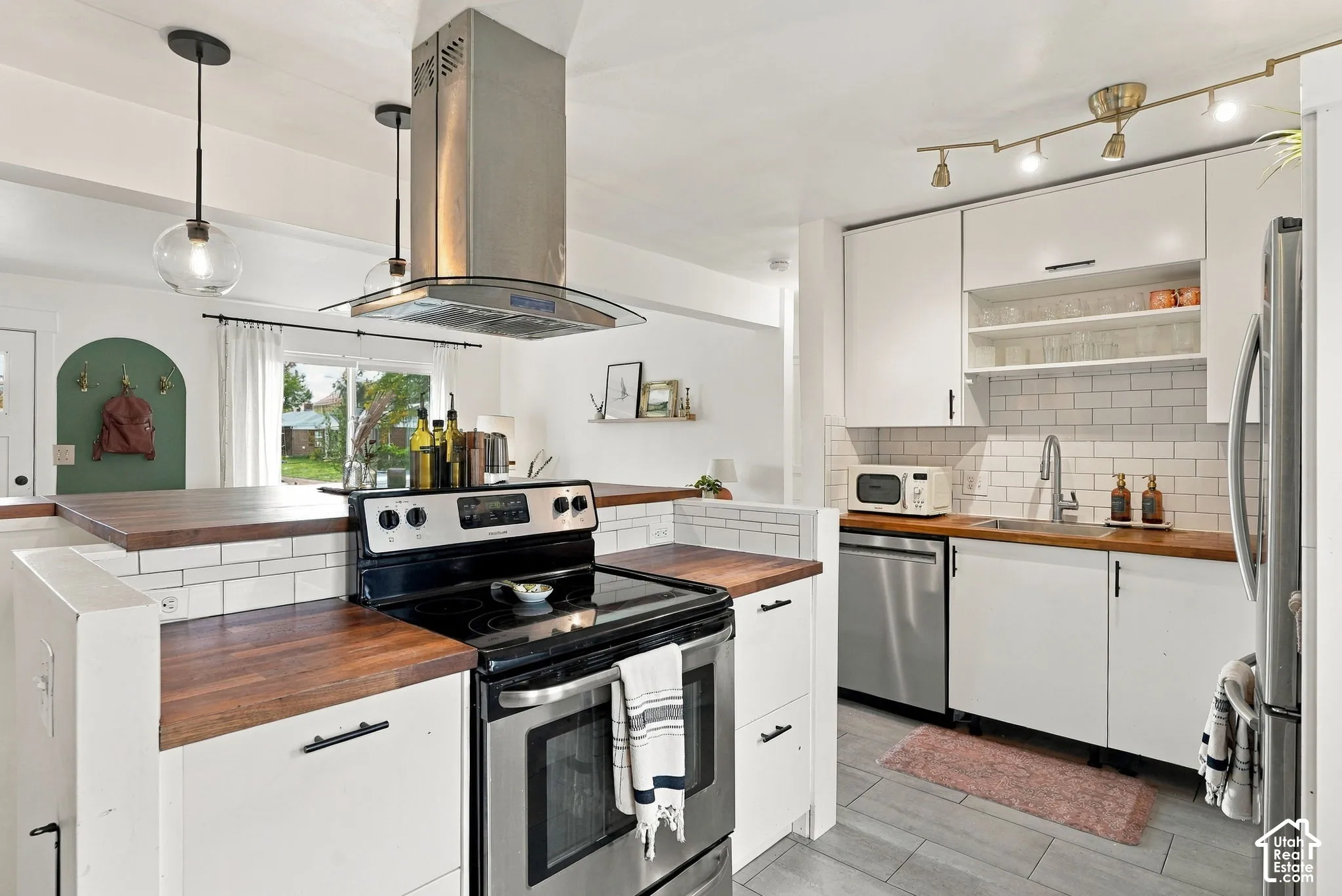 White shaker-style cabinetry with wood-finish countertops, stainless steel appliances, subway tile backsplash, and track lighting