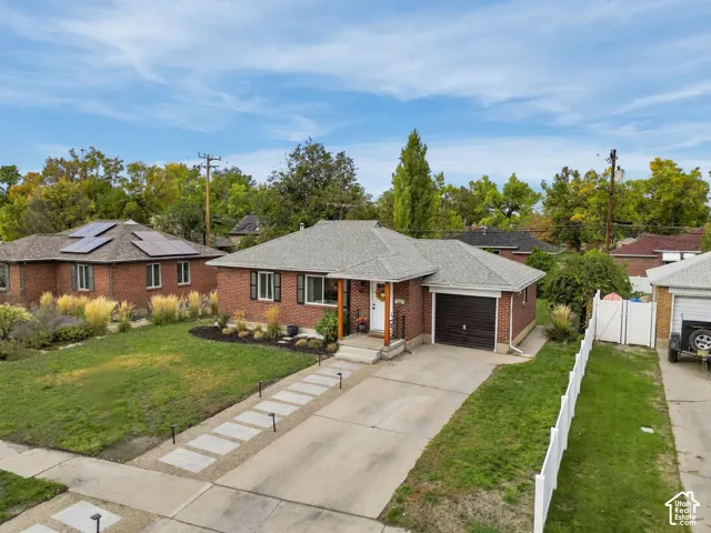 Brick exterior, attached single-car garage, concrete driveway, front lawn, and white picket fence