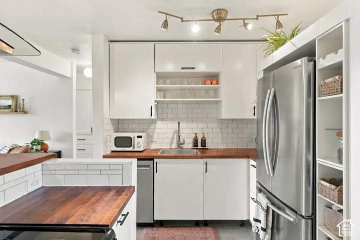 Galley kitchen featuring wood-finish countertops, white subway tile backsplash, white cabinetry with black hardware, and an integrated stainless steel refrigerator