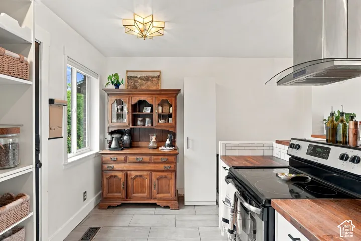 Kitchen featuring white cabinetry with black hardware, wood-finish countertops, subway tile backsplash, and a stainless steel range hood