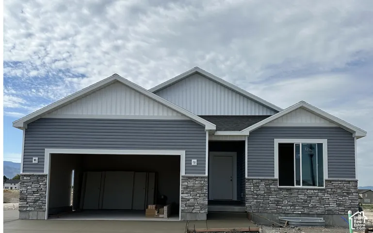 Contemporary exterior featuring grey siding, white vertical accent siding, a dark shingle roof, stone veneer accents, and an attached two-car garage