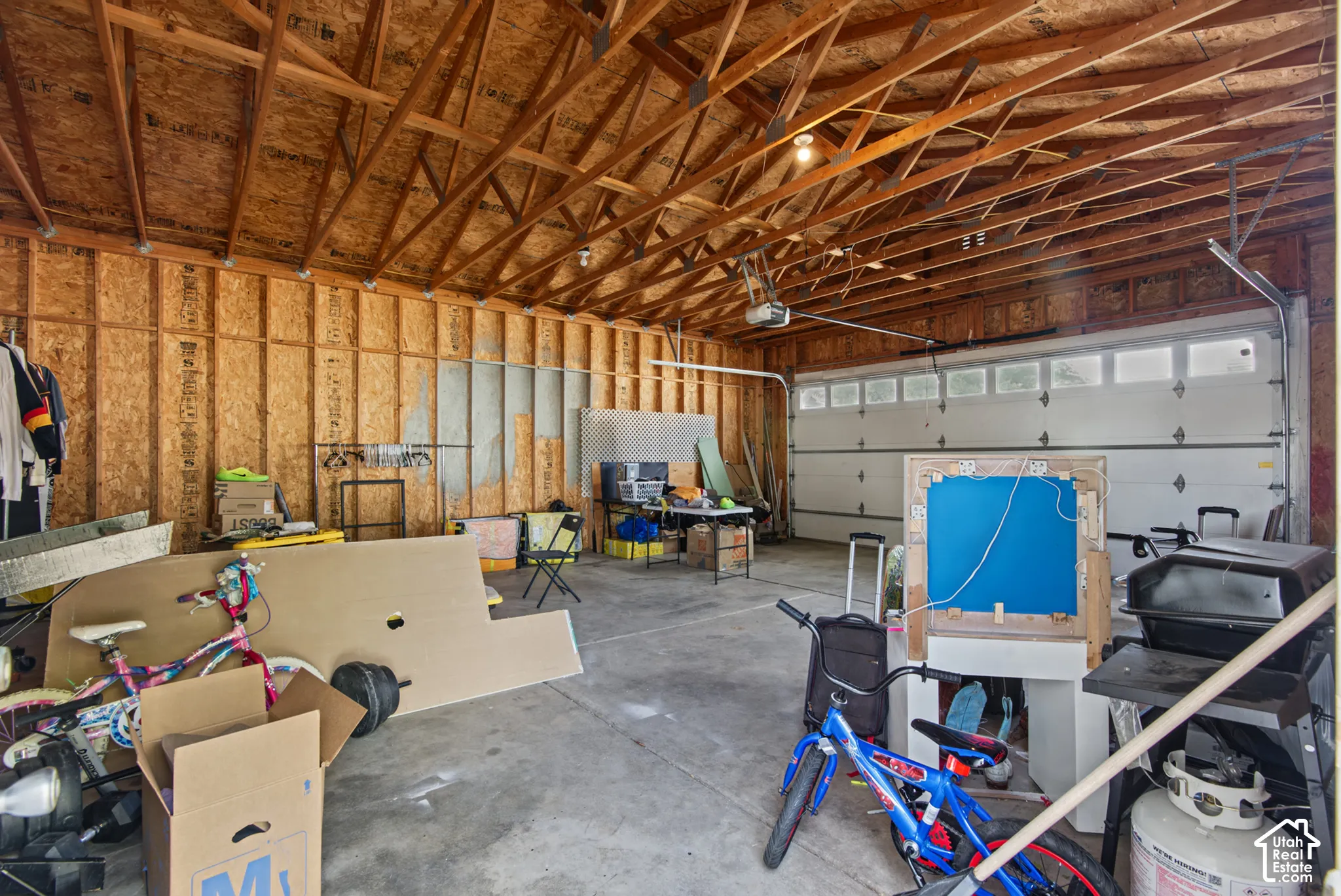 Spacious garage featuring exposed wood framing, an automatic garage door opener, and a concrete floor