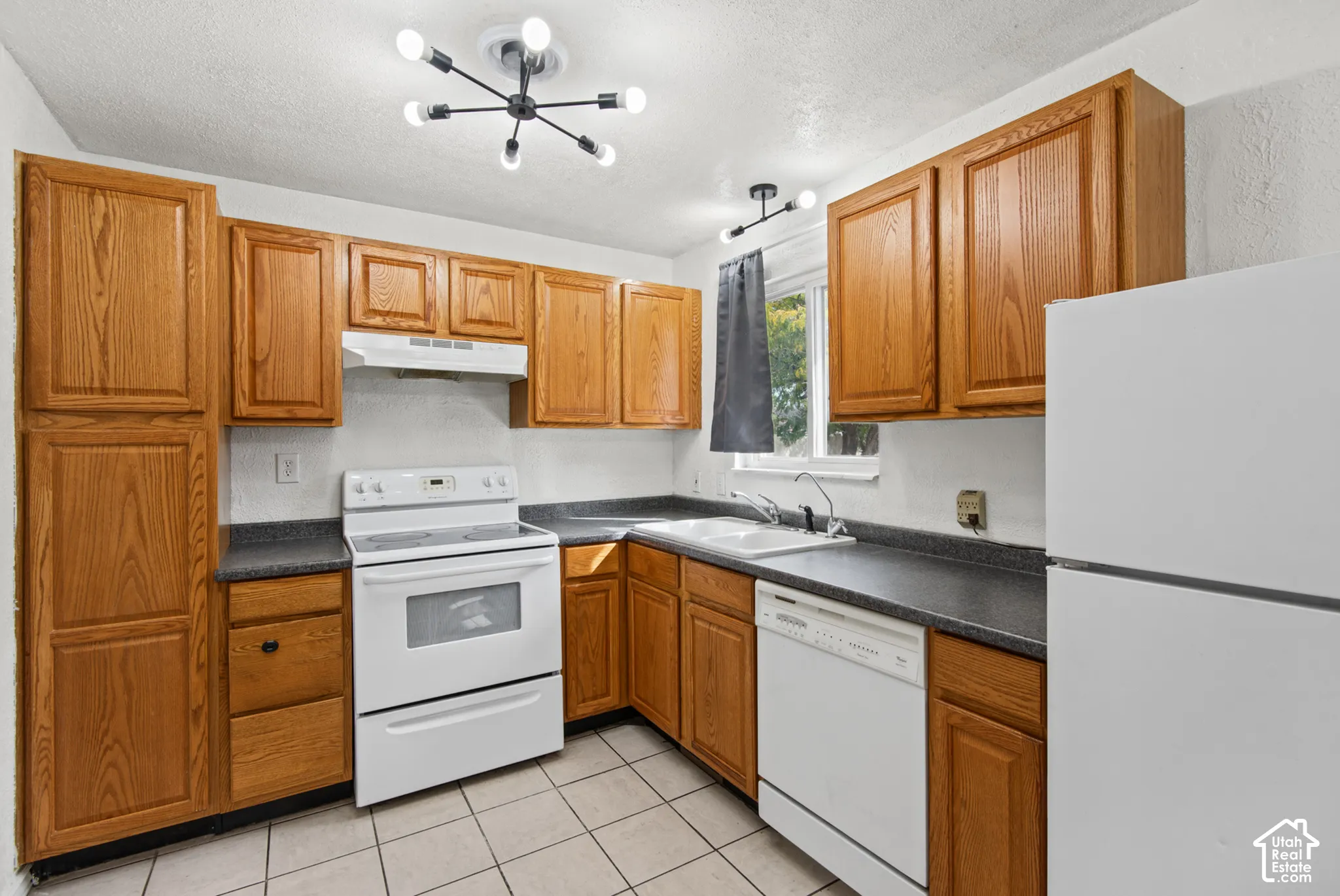 Kitchen featuring wood cabinetry, white appliances, a double basin sink, gray countertops, and tiled flooring