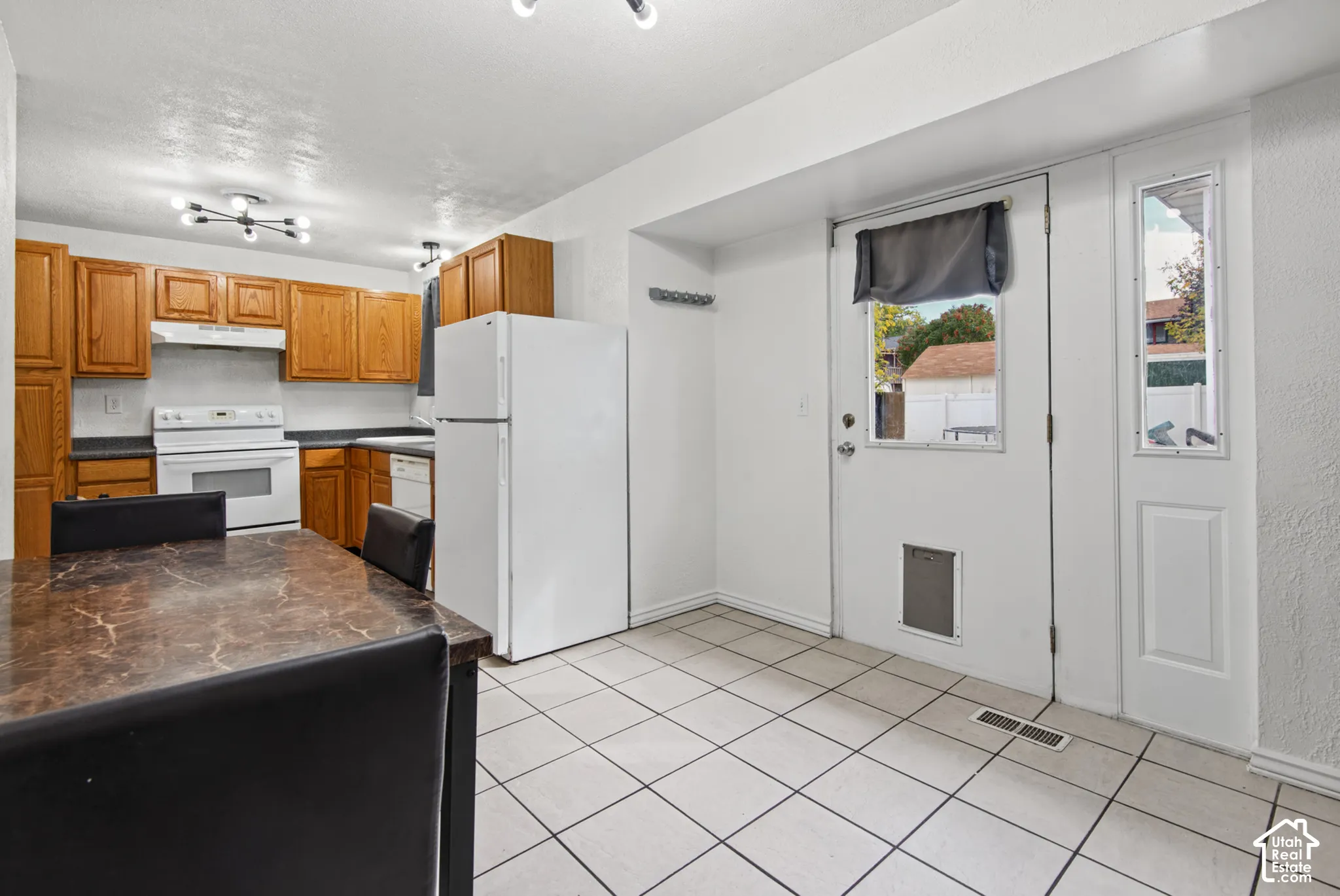 Kitchen featuring white appliances, warm wood-finish cabinetry, dark countertops, and tile flooring