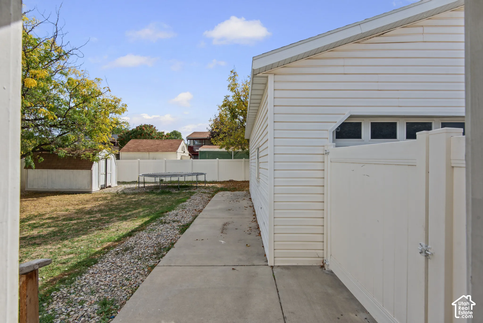 Exterior featuring white vinyl siding, a concrete pathway, a gravel strip, and a white vinyl fence