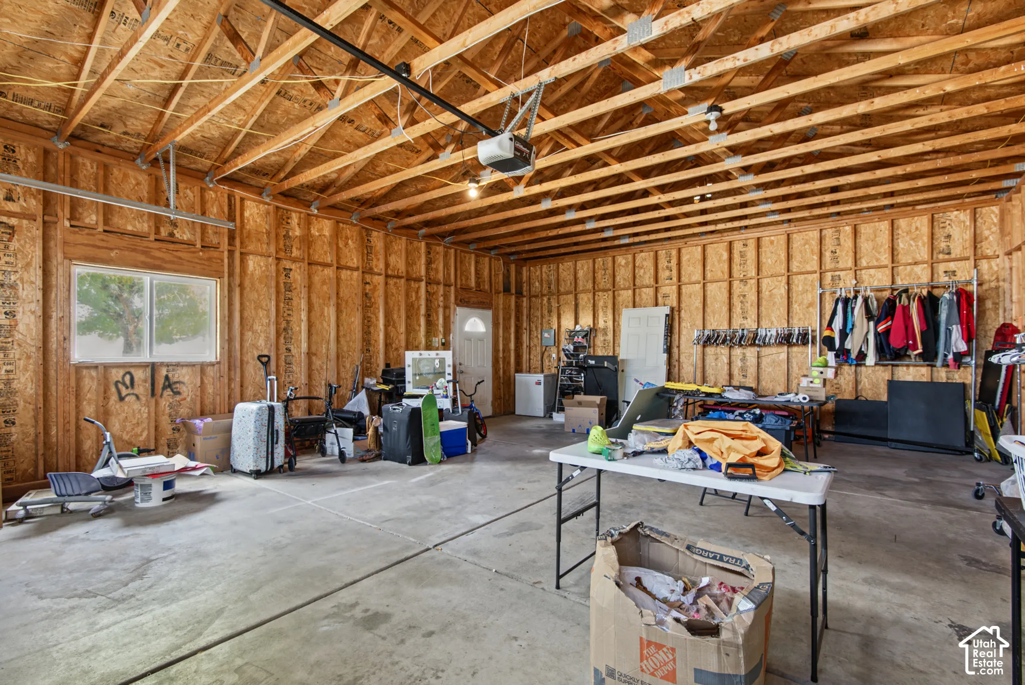 Exposed wood beam ceiling, unfinished wood panel walls, concrete flooring, dual pane window, and an interior door