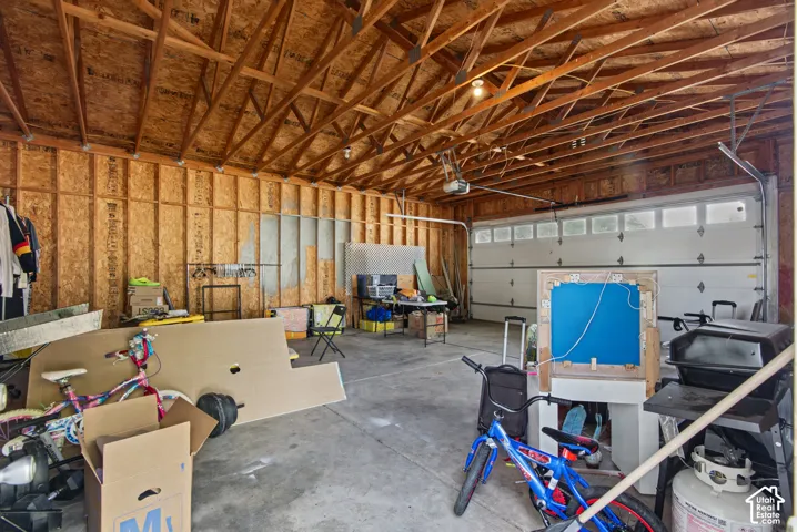 Spacious garage featuring exposed wood framing, an automatic garage door opener, and a concrete floor