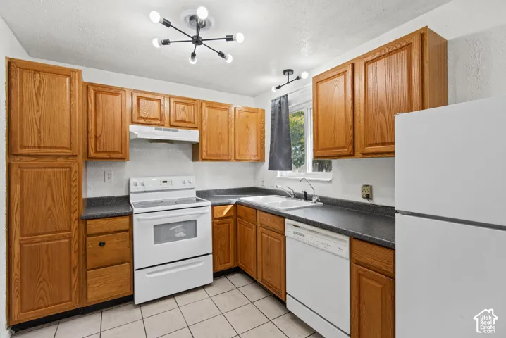 Kitchen featuring wood cabinetry, white appliances, a double basin sink, gray countertops, and tiled flooring