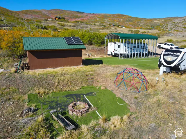 Detached shed with metal roof and solar panel, covered parking structure, and a circular stone fire pit