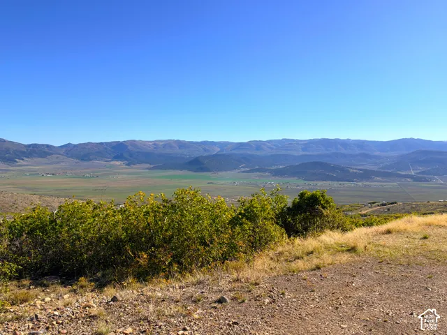 Expansive mountain backdrop with a clear blue sky, featuring a sweeping valley and distant green fields