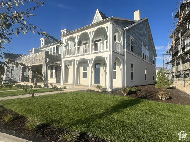 Two-story facade with light blue siding and white trim, featuring a double-tiered balcony with decorative railings, a covered porch, and a dormer