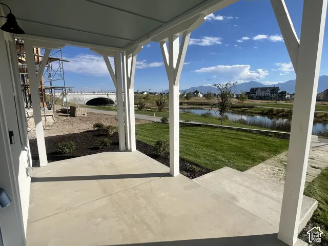 Covered porch with concrete flooring, framed by white structural posts, offering views of a landscaped pond and distant mountains