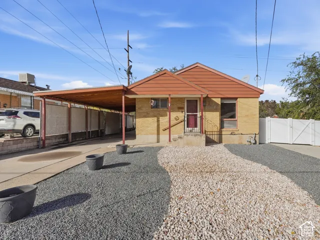Exterior featuring light-colored brick siding, attached carport with wooden ceiling, and decorative gravel landscaping
