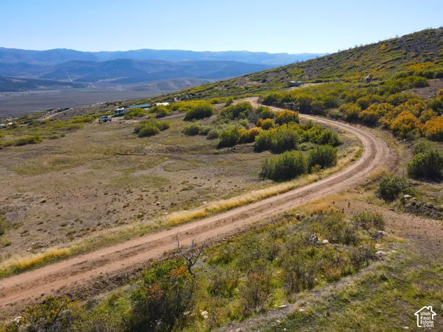 Expansive natural landscape with varied terrain, featuring a winding dirt road and distant mountain range