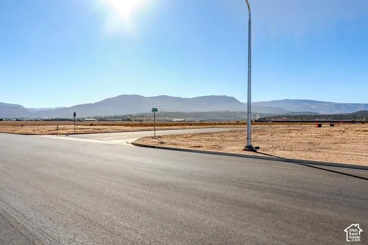 Paved road frontage, mountain backdrop, street sign, and a light pole