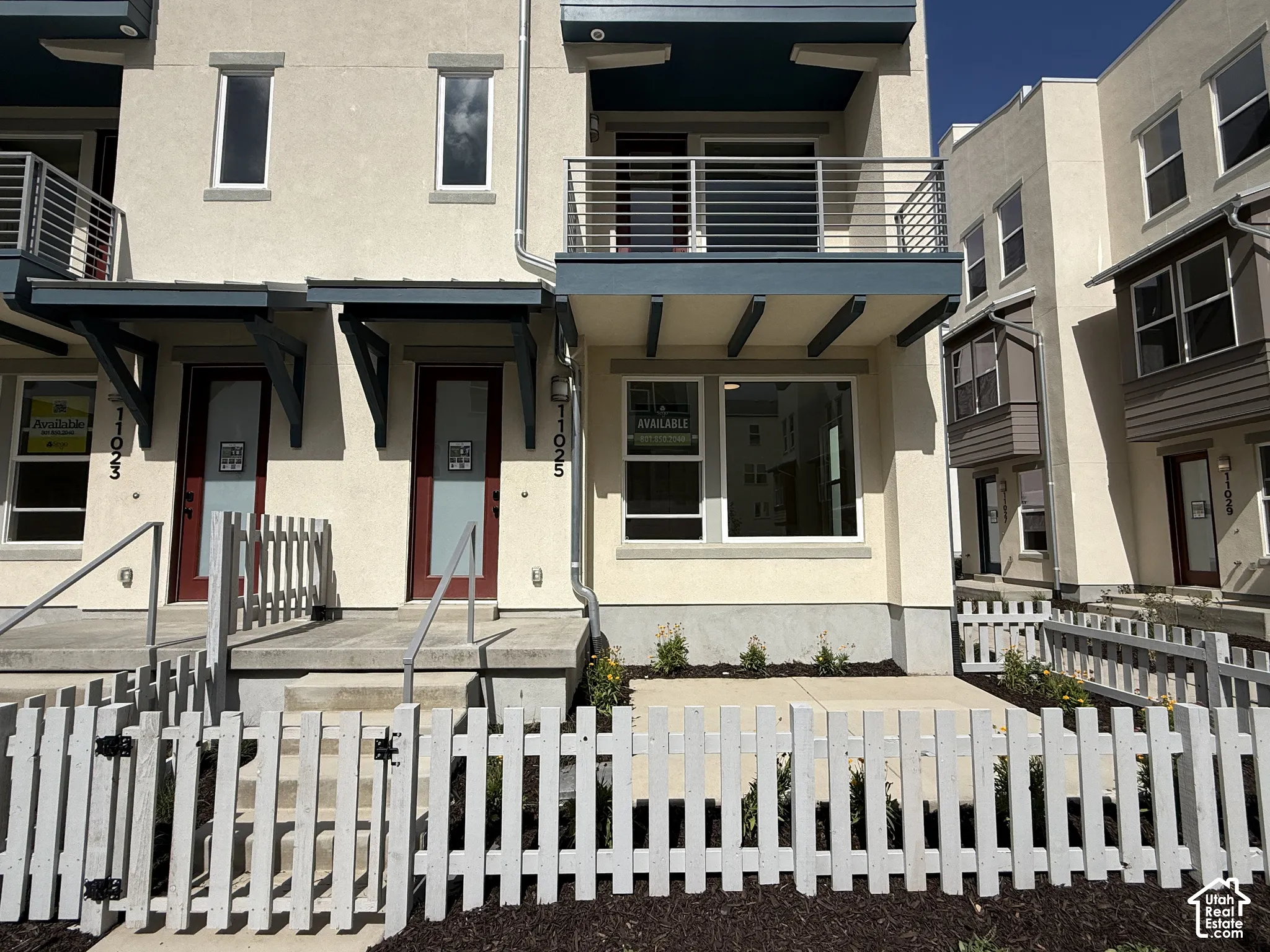 Contemporary townhome exterior with stucco finish, private balcony with metal railings, white picket fence, and covered front entryways