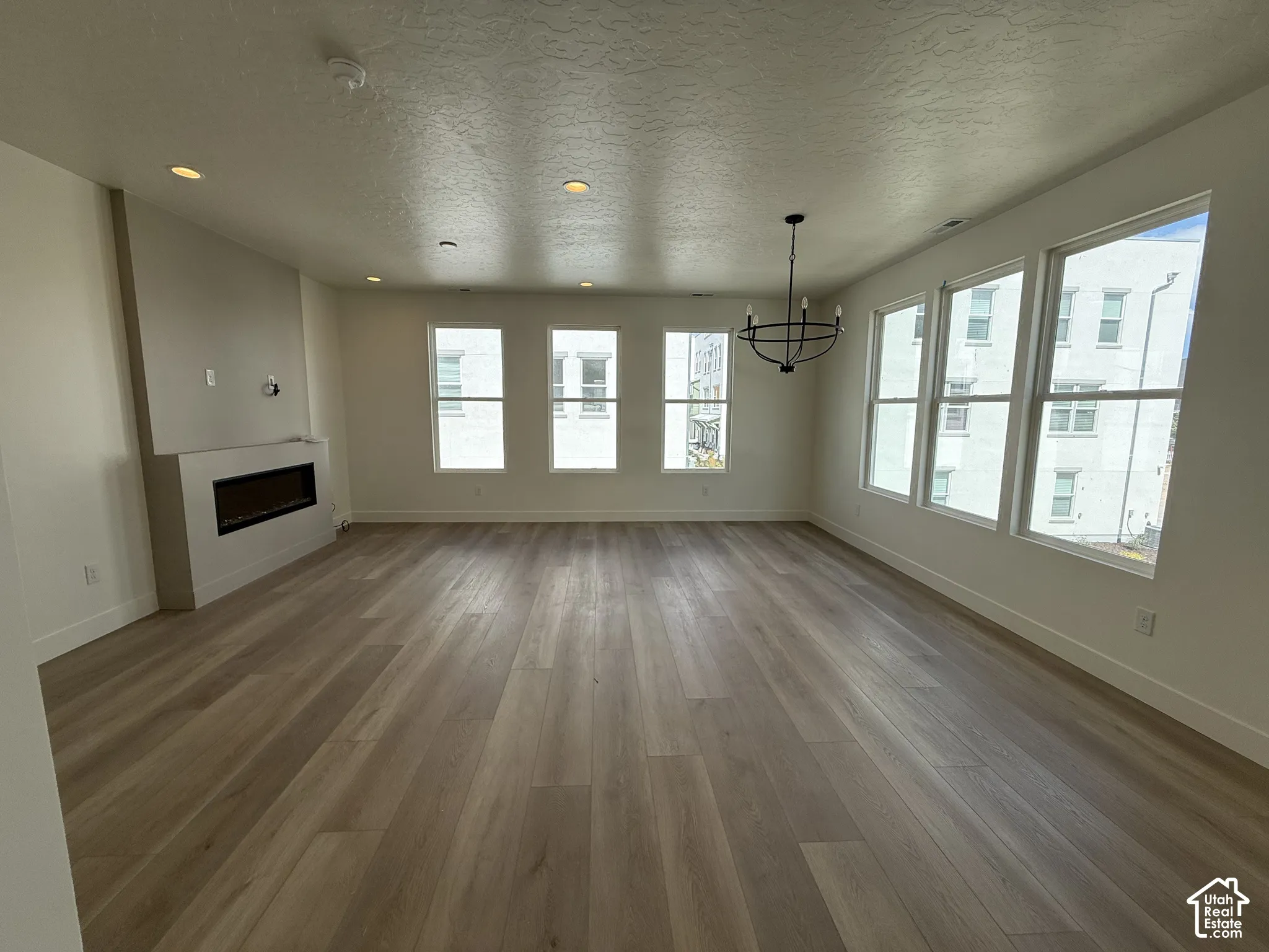 Recessed lighting, wood-finish flooring, linear fireplace, multiple windows, and a black chandelier