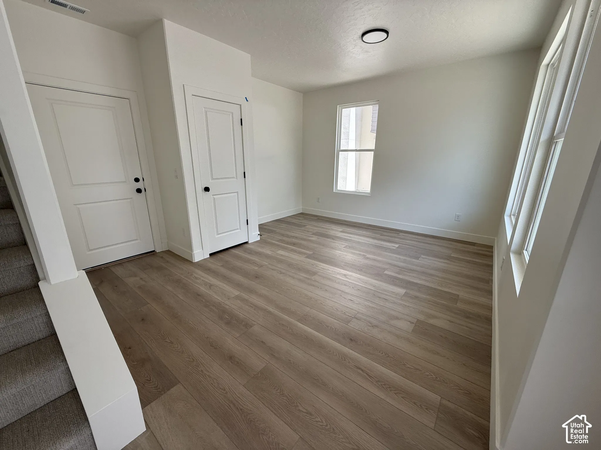 Wood-finish flooring throughout, bright white walls, contemporary ceiling light fixture, and multiple windows for natural illumination