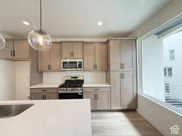 Spacious kitchen featuring light wood-finish cabinetry, quartz countertops, a gas range with a stainless steel microwave, and wood-finish flooring