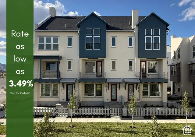 Contemporary townhome exterior with mixed siding, multiple balconies, a covered entryway, white picket fencing, and a manicured lawn