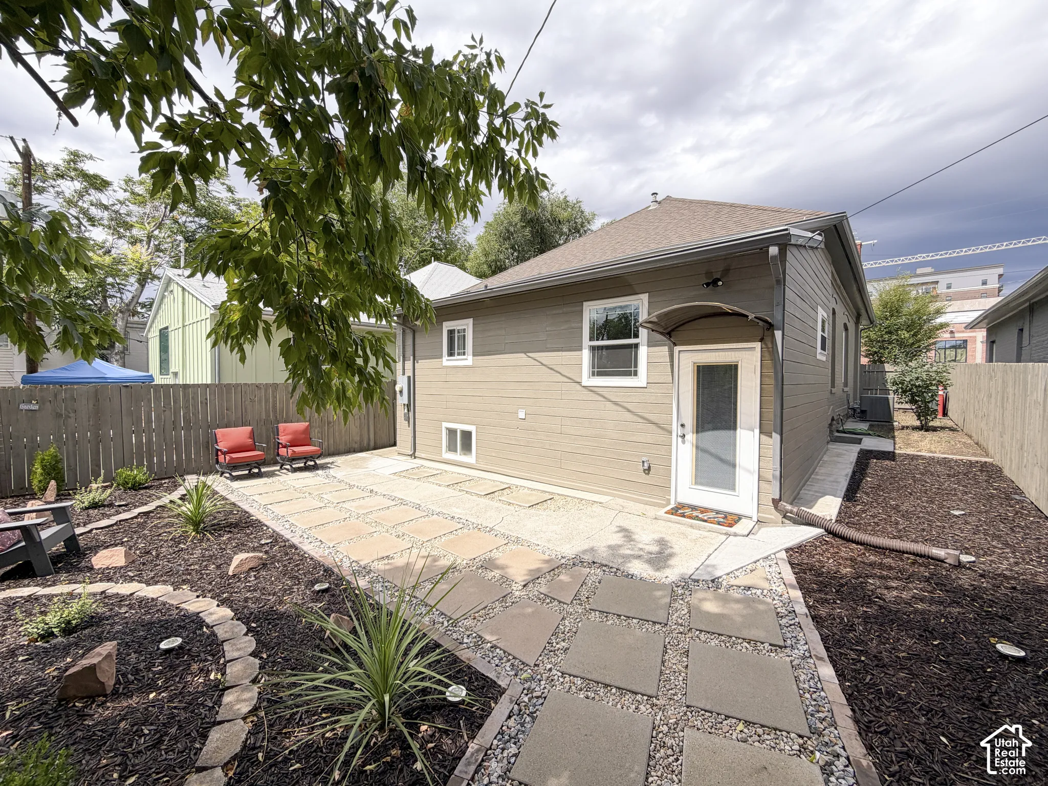 Landscaped yard with stone pavers and gravel pathway, privacy fence, and a covered entryway.