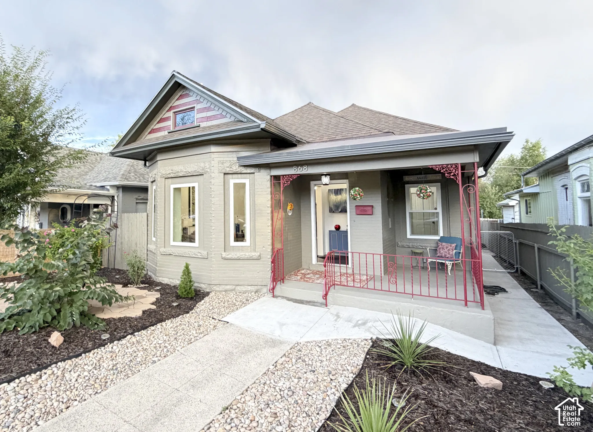 Brick Victorian featuring an inviting covered porch with bold railing, a double pane bay window, and classic roofline with architectural shingles.
