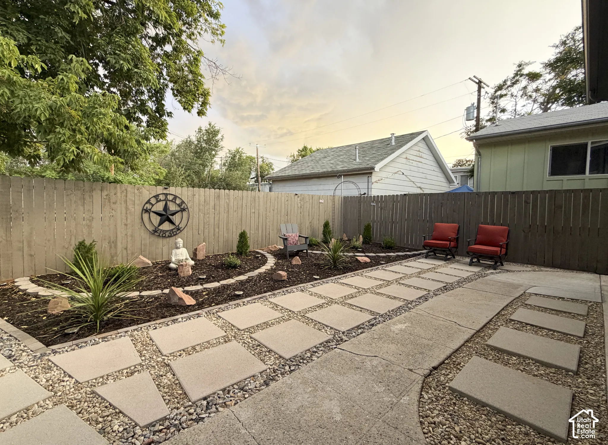 Paved patio area, stone paver walkway, landscaped garden bed, wood privacy fence.
