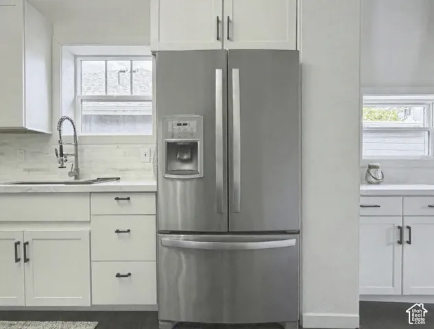 Stainless steel French door refrigerator, white shaker-style cabinetry with matte black hardware, dual windows, white countertops, and subway tile backsplash