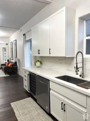 White shaker-style cabinetry with matte black hardware, stainless steel sink, pull-down faucet, and integrated wine refrigerator
