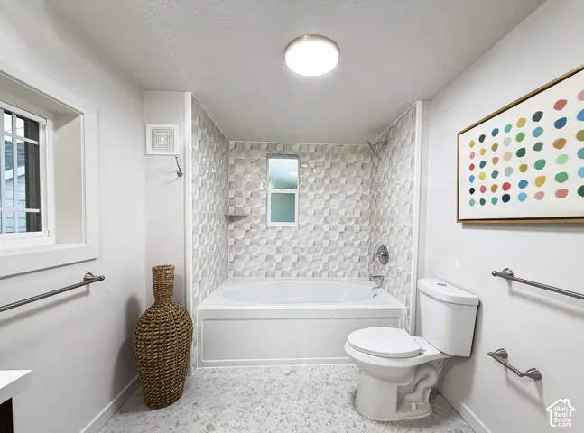 White soaking tub with a tiled surround, integrated shower, and a privacy window
