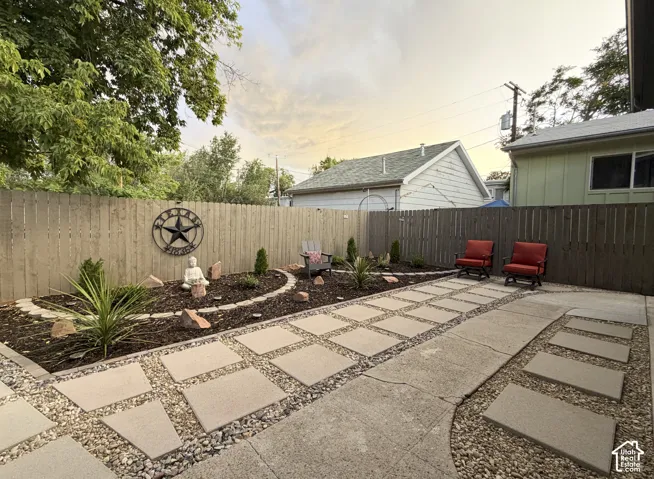 Paved patio area, stone paver walkway, landscaped garden bed, wood privacy fence.