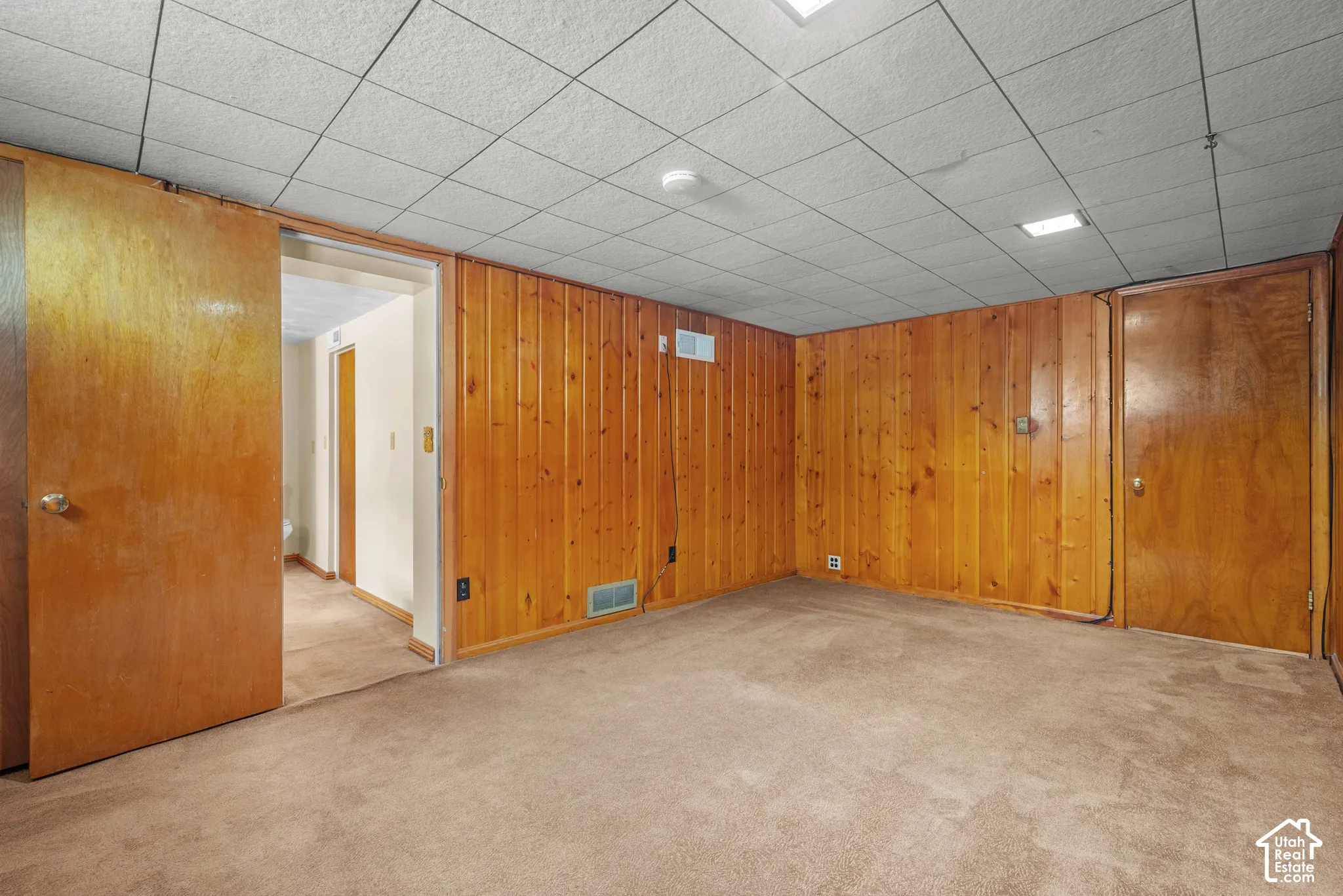 Wood paneling, carpet flooring, drop ceiling, recessed lighting, and a sliding wood door