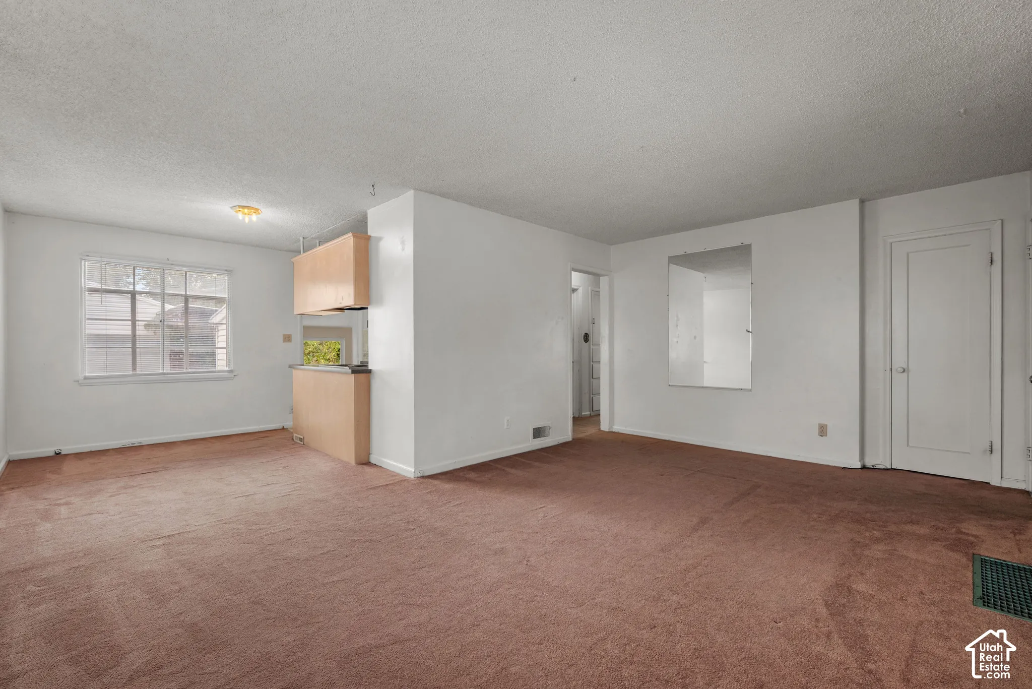 Spacious room with plush carpeting, natural light from a multi-pane window, and a built-in pass-through with upper cabinetry