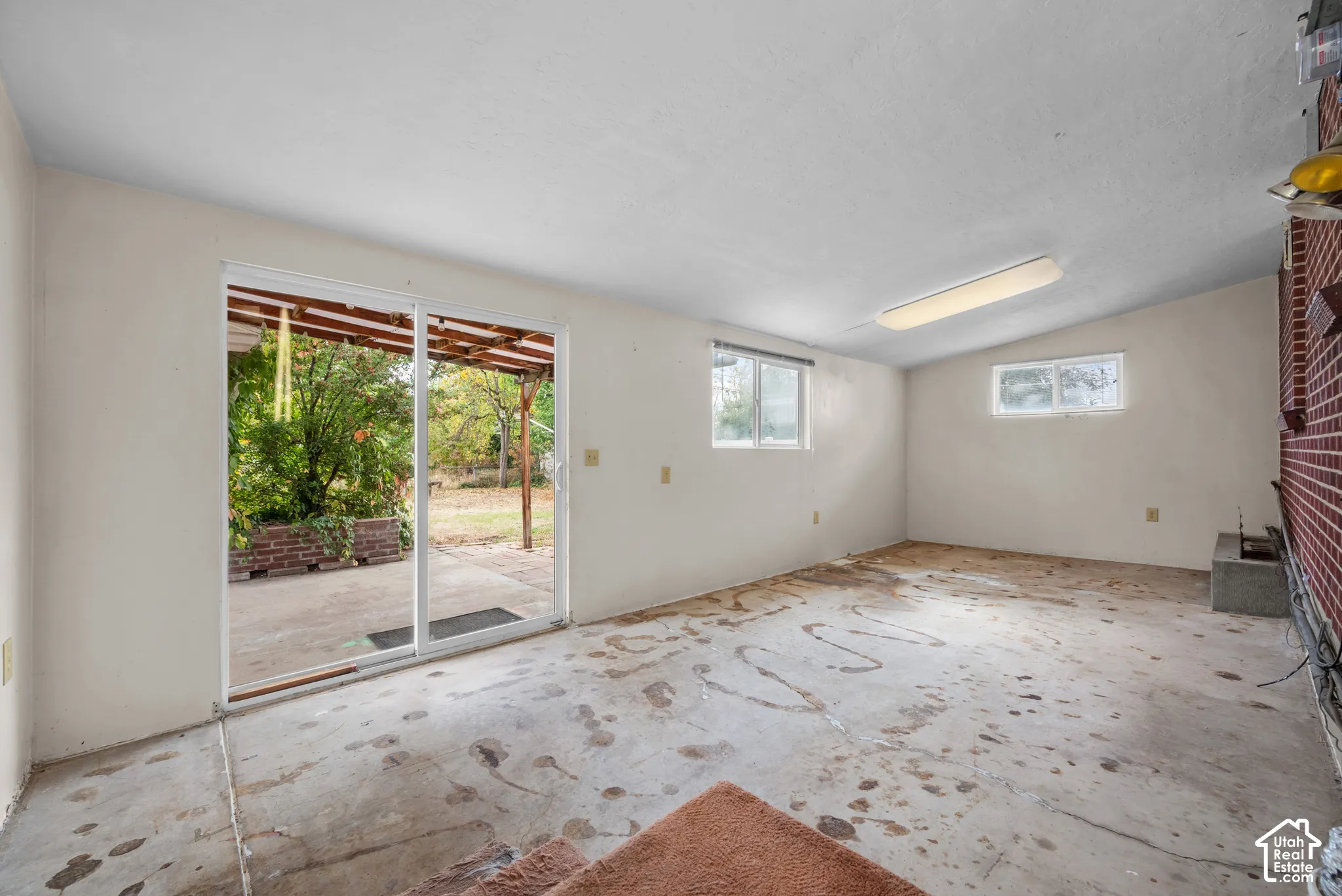 Interior space with concrete flooring, multiple windows, and a sliding glass door leading to an outdoor patio with a brick planter