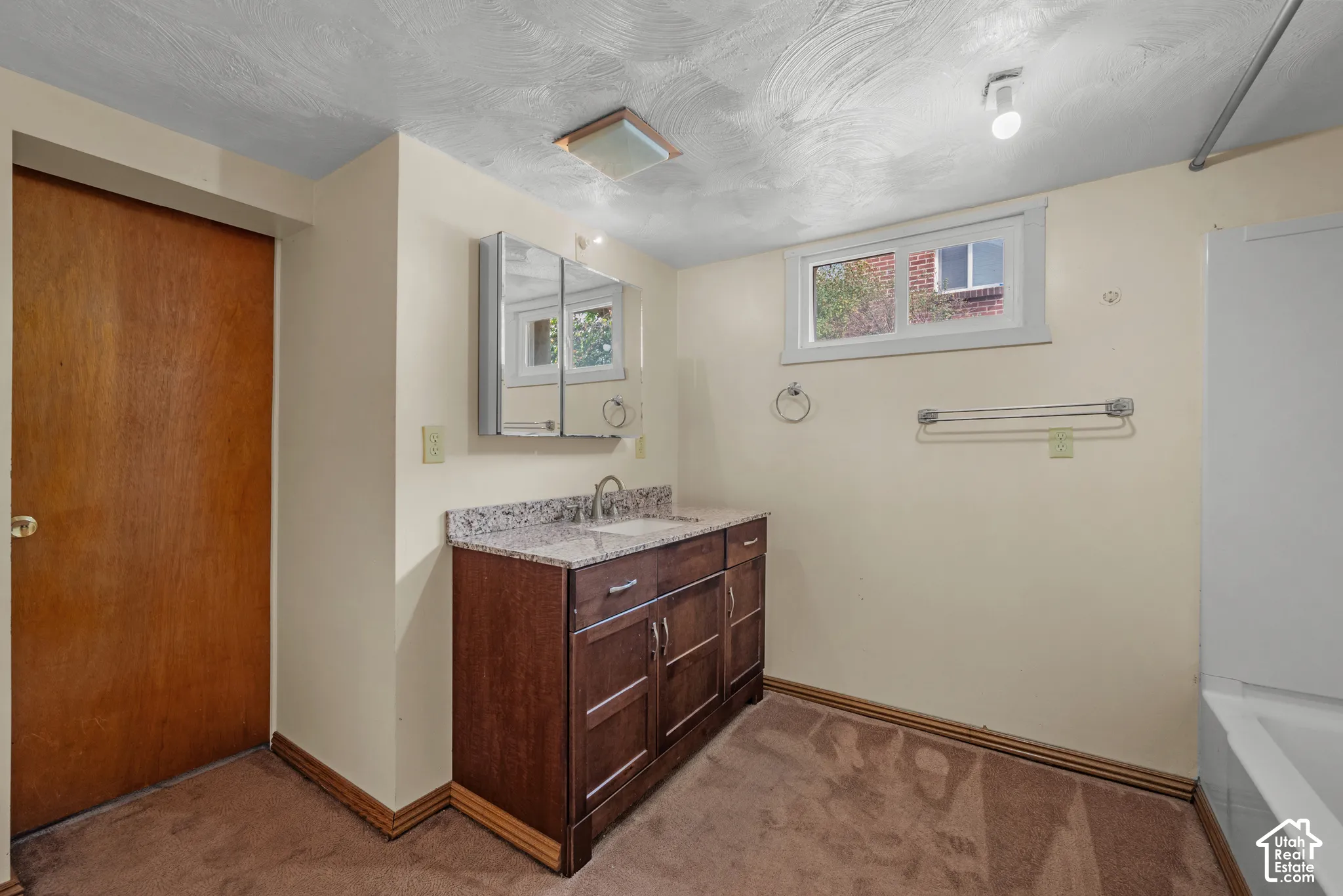 Bathroom featuring a wood-finish vanity with a stone countertop, a sink with a chrome faucet, and a mirrored medicine cabinet