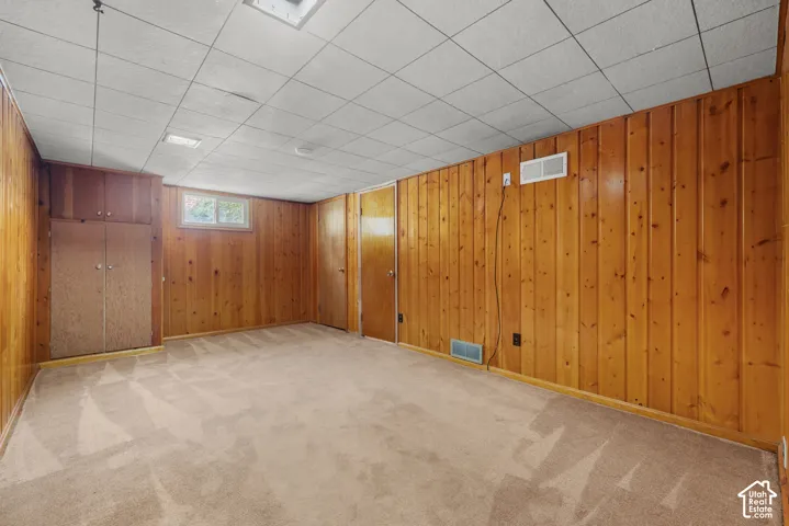 Carpeted flooring, wood paneling, built-in storage, and a drop ceiling with recessed lighting
