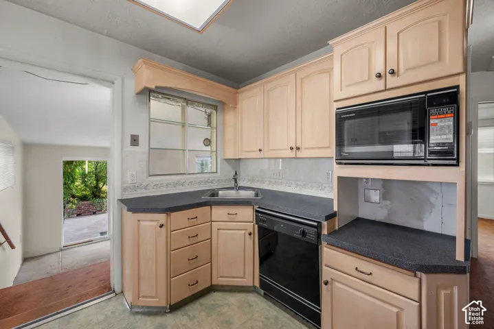 Light wood-finish cabinetry with black hardware, black microwave, black dishwasher, and a corner sink with a single-handle faucet