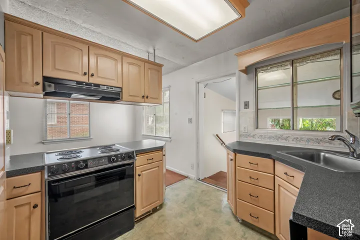 Hardwood cabinetry, black countertops, stainless steel sink, black range oven, and a recessed ceiling light fixture